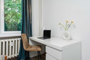 Ein moderner Büroraum mit weißem Schreibtisch, einem Laptop, einem Stuhl, einer Vase mit Blumen und einem Fenster mit Vorhängen.