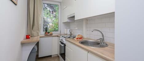 A compact kitchen with white cabinets, a wooden countertop, a stainless steel sink, and a window with a view of greenery.