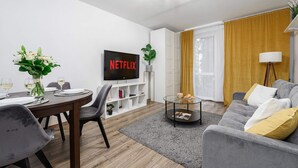 A modern living room with a dining area, a flat-screen TV, a bookshelf, and a sofa with cushions. - Lush Stay on Przasnyska (Warszawa 2)