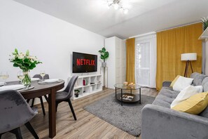 Ein modernes Wohnzimmer mit Essbereich, einem Flachbildfernseher, einem Bücherregal und einem Sofa mit Kissen.