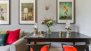 Uma área de refeições com mesa de madeira escura, cadeiras, um vaso com flores e quadros nas paredes.