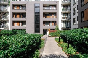 A multi-story residential building with balconies, a central glass facade, and a well-maintained garden pathway. - Quiet Flat with Garage (Warszawa 2)