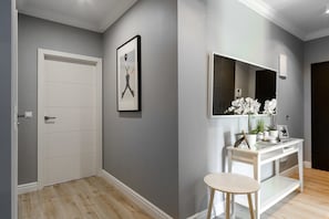 Ein Flur mit einer weißen Tür, einem gerahmten Bild an der Wand, einem weißen Waschtisch mit Spiegel und einem kleinen Hocker.