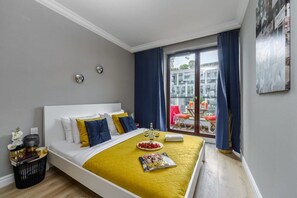 Ein Hotelzimmer mit einem Bett, einem kleinen Tisch mit einer Zeitschrift, einer Flasche und Gläsern sowie einem Balkon mit Tisch und Stühlen.
