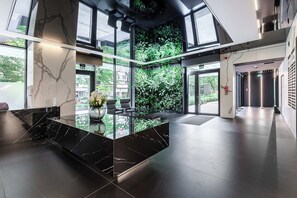 Eine moderne Lobby mit einem Marmor-Rezeptionsschalter, einer Glastrennwand und Blick auf Grünflächen.