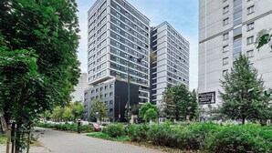 A modern high-rise building with a glass facade, surrounded by greenery and a paved walkway. - Lush Home near Varso Tower (Warszawa)