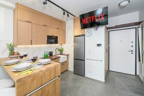 A modern kitchen with wooden cabinets, a microwave, a refrigerator, and a wall-mounted TV displaying 'NETFLIX'. - Lush Home near Varso Tower (Warszawa)