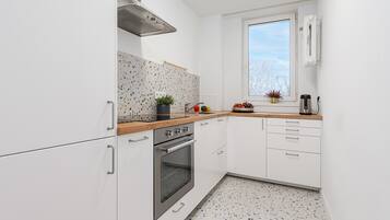 A modern kitchen with white cabinetry, a stainless steel oven, a window with a view, and a countertop with a plant and fruit.
