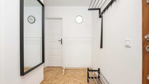 A hallway with a wooden parquet floor, a white door, and a bench with metal bars. There are two wall-mounted clocks and a light switch on the wall. - Magnificent Beach House for 6 (Warszawa)