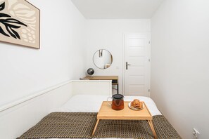 Ein kleines, aufgeräumtes Schlafzimmer mit Bett, Nachttisch und Spiegel.