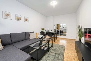 Un salon moderne avec un canapé gris, une table basse en verre et un coin repas avec une table dressée pour deux personnes.