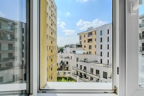 Blick aus einem Fenster eines Mehrfamilienhauses mit Balkonen und blauem Himmel.