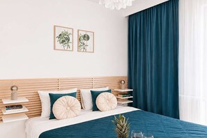 A modern bedroom with a bed, bedside tables, a nightstand, a potted plant, and a window with curtains. - Renovated Coastal Stone House in Lanildut (Łódź)