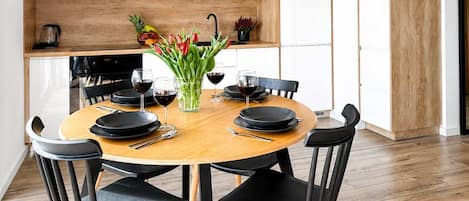 A modern dining area with a round wooden table, black chairs, and a vase of flowers.