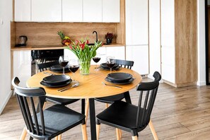 A modern dining area with a round wooden table, black chairs, and a vase of flowers. - Renovated Coastal Stone House in Lanildut (Łódź)