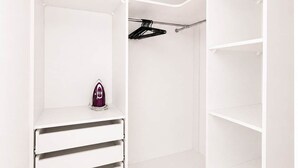 Een witte kast met open planken, een kledingroede en een klein paars apparaat.