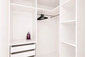 A white closet with open shelves, a hanging rod, and a small purple appliance. - Renovated Coastal Stone House in Lanildut (Łódź)