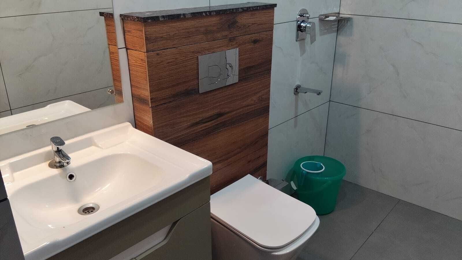 Baño con lavamanos, inodoro y un bote de basura verde.