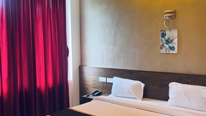 A hotel room with a bed, a nightstand, a phone, a wall-mounted light, and a ceiling fan. - MASBAH RESIDENCY (Mananthavady)