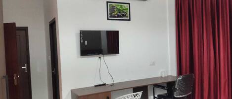 A room with a flat-screen TV mounted on the wall, a desk with a chair, and a door.