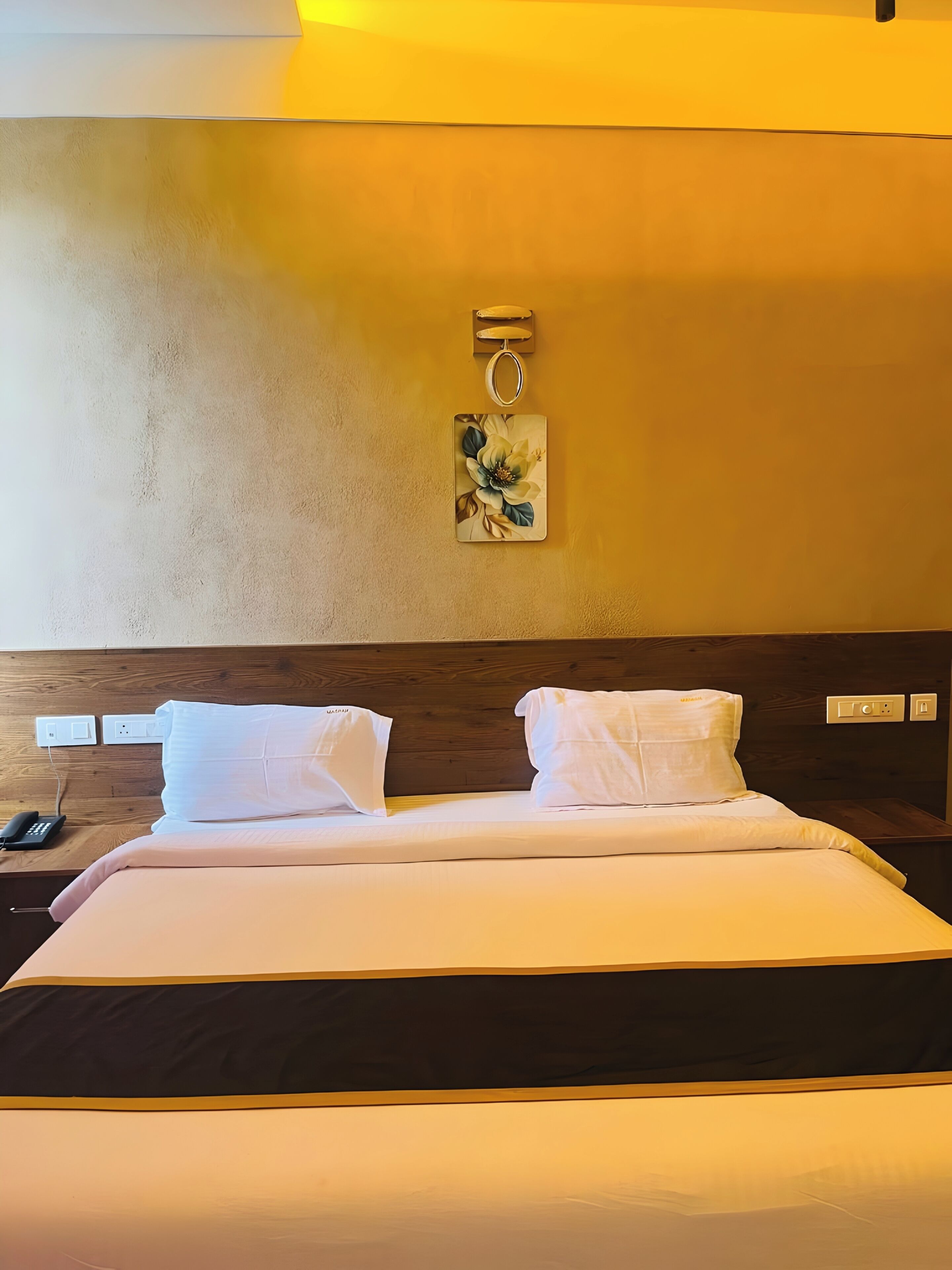 A hotel room with a bed, a nightstand with a phone, and a wall-mounted light fixture.