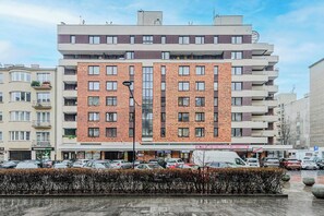 A multi-story building with a brick facade, several balconies, and a row of shops at the ground level. - Warsaw Apartment with Panoramic City Views (Warszawa 2)