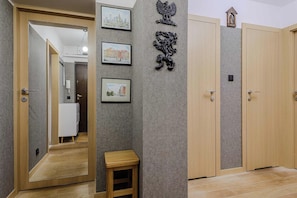 A hallway with a wooden door, a small wooden stool, and three framed pictures on the wall. - Warsaw Apartment with Panoramic City Views (Warszawa 2)