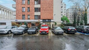 A parking lot with several cars, a building with a sign for 'Instytut Urody,' and a tree with yellow flowers. - Beachfront Villa with Panoramic Sea Views (Warszawa 2)