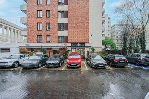 Ein Parkplatz mit mehreren Autos, ein Gebäude mit einem Schild für 'Instytut Urody' und ein Baum mit gelben Blüten.