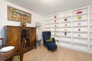 Ein Esszimmer mit gedecktem Tisch, einem blauen Sessel, einem Holzschrank und einer weißen Regalwand.