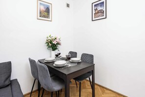 Un coin repas avec une table en bois foncé, dressée pour quatre personnes, entourée de chaises à revêtement gris.