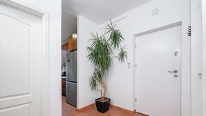 A hallway with a potted plant, a white door, and a kitchen area in the background.