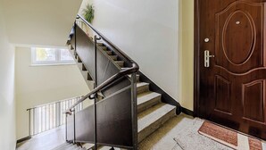 A staircase with a metal handrail leading to a landing, a wooden door with a doorknob, and a small window with a view of trees.