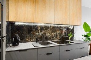 A modern kitchen with a black marble backsplash, a coffee maker, a sink, and a plant. - Historic City Stay for 4 in Warsaw (Łódź)