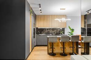 A modern kitchen with a marble backsplash, wooden cabinets, and a bar area with bar stools. - Accessible Apartment Stay in Łódź City (Łódź)