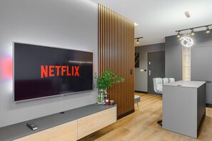 A modern living room with a large flat-screen TV displaying 'NETFLIX', a wooden slat wall, a small plant, and a grey sofa. - Historic City Stay for 4 in Warsaw (Łódź)