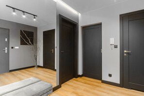 A modern hallway with dark doors, a bench, and a vase with branches. - Historic City Stay for 4 in Warsaw (Łódź)