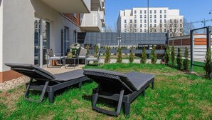 Een moderne buitenzitplaats met lounge fauteuils en een tafel, omgeven door een verzorgd gazon en een gebouw met meerdere ramen.