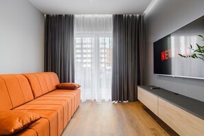 Een moderne woonkamer met een bank, een televisie en uitzicht door dunne gordijnen.