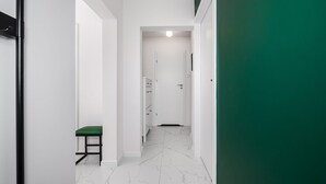 Um corredor com um banco verde, paredes brancas e uma porta no final.