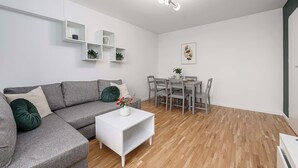 Uma sala de estar moderna com um sofá cinzento, mesa de centro branca e uma área de jantar com cadeiras e mesa cinzas.