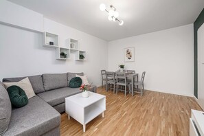 Ein modernes Wohnzimmer mit grauem Sofa, weißem Couchtisch und einem Essbereich mit grauen Stühlen und einem Tisch.