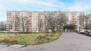 Um edifício residencial com vários andares e varandas, um caminho pavimentado e carros estacionados.