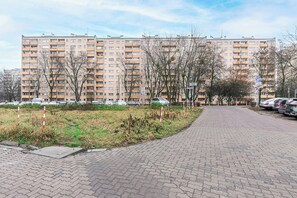 Ein Mehrfamilienhaus mit mehreren Etagen und Balkonen, ein gepflasterter Weg und abgestellte Autos.