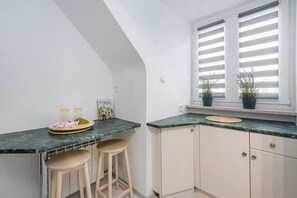 Eine Küche mit Marmorarbeitsplatte, zwei Barhocker, einem Blumentopf und einem Fenster mit Jalousien.
