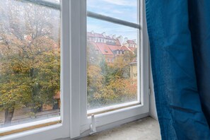 Ein Fenster mit Blick auf Gebäude und Bäume, ein teilweise geöffneter Vorhang und ein weißer Fensterrahmen.