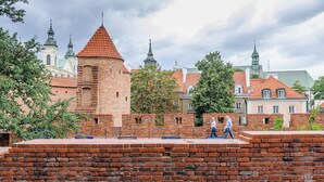 Historiallinen tiilimuuri, jossa on torni, ja sen ympärillä on puita sekä perinteisiä punatiilikattoisia rakennuksia.