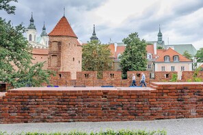 Eine historische Ziegelmauer mit einem Turm, umgeben von Bäumen und traditionellen Gebäuden mit roten Ziegeldächern.