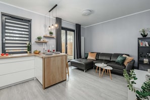 A modern living room with a sofa, a coffee table, and a kitchen area with a counter and cabinets. - 2-Bedroom Home with Balcony (Warszawa 2)