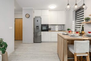 A modern kitchen with stainless steel appliances, a wooden dining table, and pendant lighting. - 2-Bedroom Home with Balcony (Warszawa 2)
